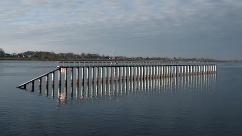 Barrière ou jetée partiellement submergée dans l’eau calme, avec mirroring sur la surface et horizon lointain. d
