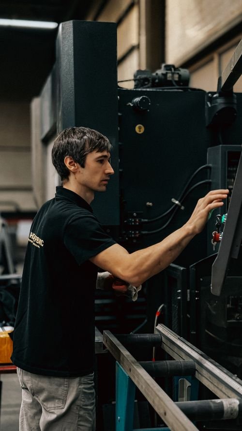 Ouvrier en usine utilisant une machine industrielle, cadrage de profil dans un environnement manufacturier. coeﬃt du travail en roumanie mentionné dans le contexte.